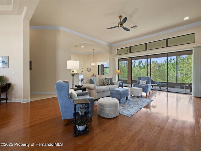 living area featuring baseboards, visible vents, arched walkways, wood finished floors, and crown molding