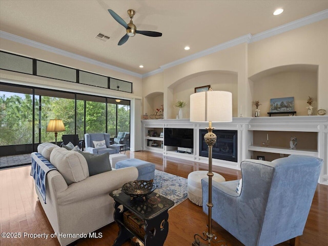 living area with a glass covered fireplace, visible vents, crown molding, and wood finished floors