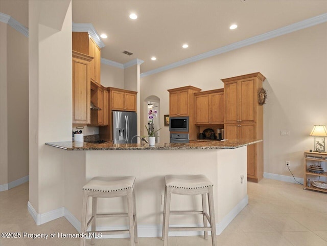 kitchen featuring wall oven, a peninsula, built in microwave, dark stone counters, and stainless steel fridge