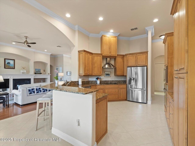 kitchen with visible vents, appliances with stainless steel finishes, open floor plan, a peninsula, and wall chimney range hood