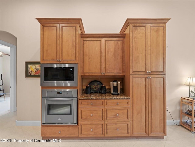 kitchen with brown cabinets, built in microwave, stainless steel oven, and dark stone counters