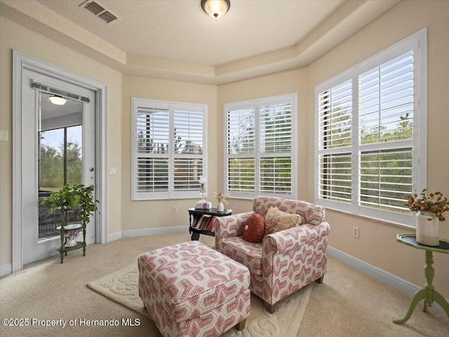 living area with a tray ceiling, visible vents, light carpet, and baseboards