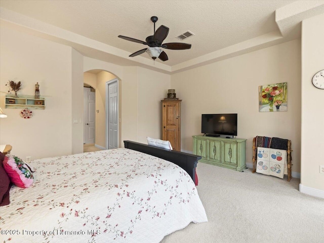 carpeted bedroom featuring arched walkways, a raised ceiling, visible vents, and a textured ceiling