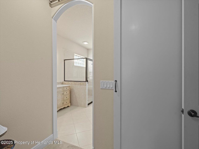 hallway featuring arched walkways and light tile patterned flooring