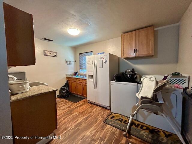 kitchen featuring light wood-style flooring, white fridge with ice dispenser, visible vents, and light countertops