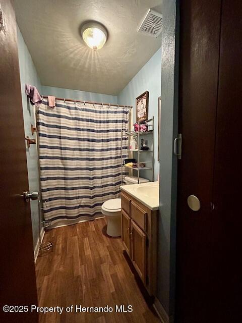 bathroom with visible vents, a shower with shower curtain, toilet, wood finished floors, and vanity