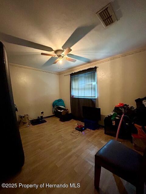 bedroom featuring ornamental molding, wood finished floors, visible vents, and a ceiling fan