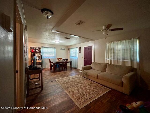 living room with dark wood-style floors, visible vents, and a ceiling fan