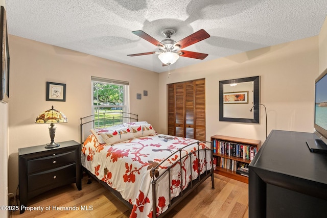 bedroom with a closet, ceiling fan, a textured ceiling, and light wood-style floors