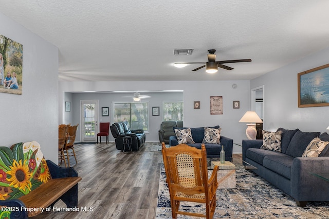 living room with a ceiling fan, wood finished floors, visible vents, and a textured ceiling