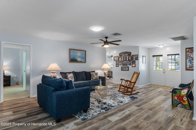 living room with visible vents, a textured ceiling, wood finished floors, french doors, and baseboards