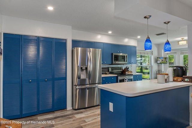 kitchen featuring visible vents, pendant lighting, light wood-style flooring, blue cabinetry, and appliances with stainless steel finishes