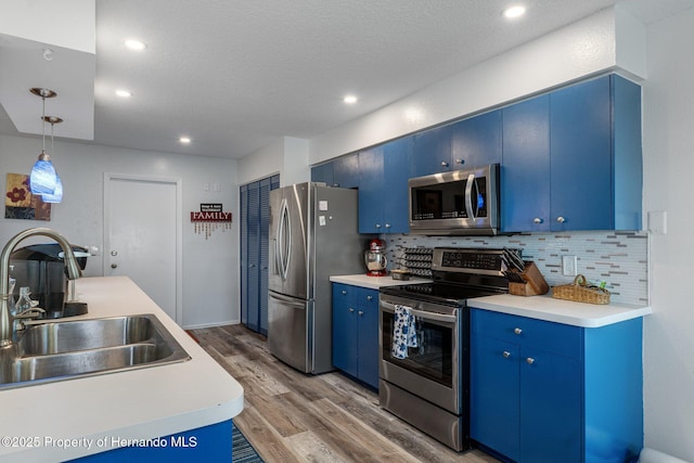 kitchen featuring light wood finished floors, a sink, appliances with stainless steel finishes, blue cabinets, and tasteful backsplash