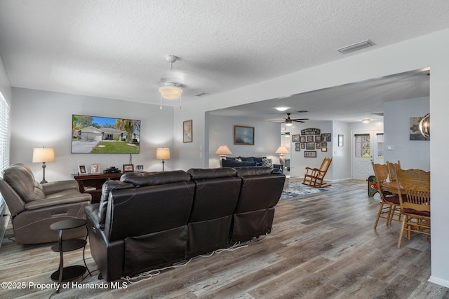 living room featuring visible vents, a textured ceiling, ceiling fan, and wood finished floors