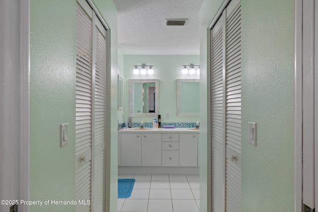 bathroom featuring tile patterned floors, a closet, a textured ceiling, and double vanity