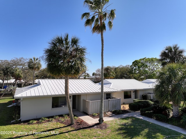 view of front facade featuring metal roof, a front lawn, a standing seam roof, and stucco siding