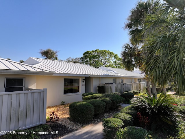 back of house with a standing seam roof, metal roof, fence, and stucco siding