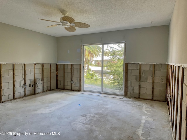 unfurnished room with concrete block wall, a textured ceiling, unfinished concrete floors, and a ceiling fan