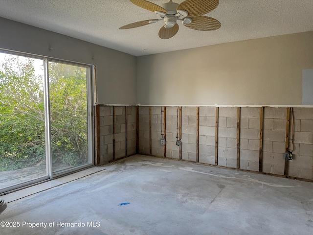 spare room featuring a ceiling fan, a textured ceiling, concrete flooring, and concrete block wall