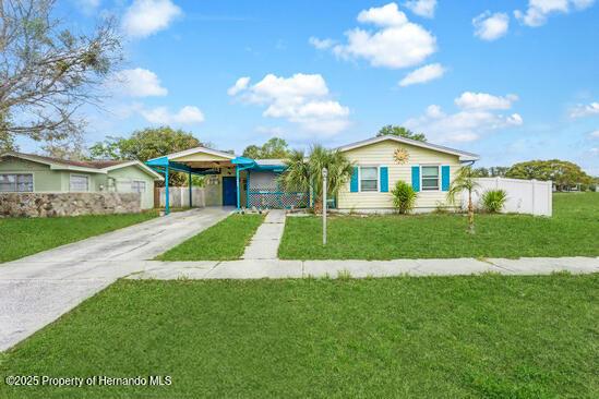 view of front facade with concrete driveway, a carport, a front yard, and fence