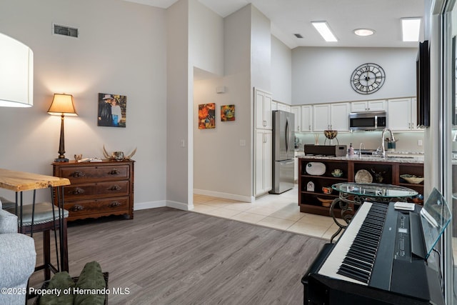 kitchen with visible vents, light wood-style flooring, stainless steel appliances, a high ceiling, and white cabinets