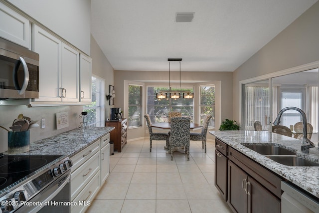 kitchen with vaulted ceiling, stainless steel appliances, light tile patterned flooring, white cabinetry, and a sink