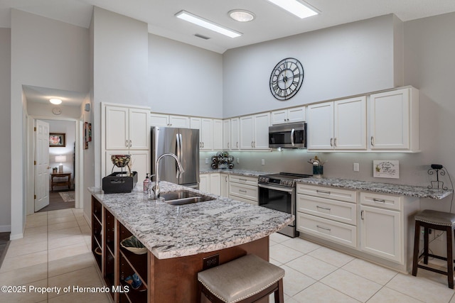 kitchen featuring light tile patterned floors, a sink, a towering ceiling, appliances with stainless steel finishes, and a kitchen bar