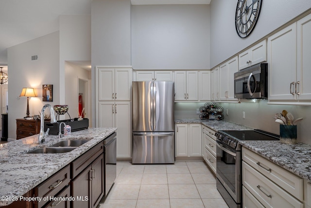 kitchen featuring light tile patterned floors, light stone countertops, a sink, a towering ceiling, and appliances with stainless steel finishes