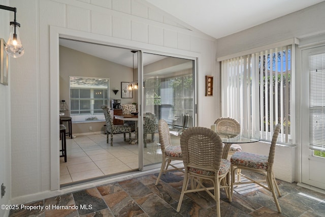 dining room with an inviting chandelier, stone finish flooring, and lofted ceiling