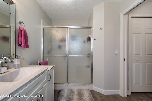 full bath with baseboards, a stall shower, wood finished floors, a textured ceiling, and vanity