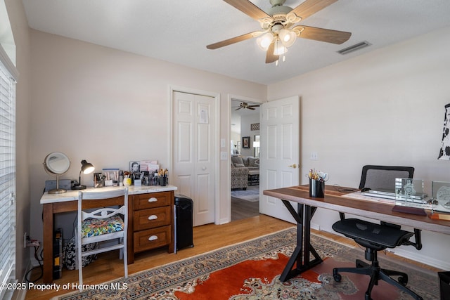 office area with light wood-style floors, visible vents, and ceiling fan