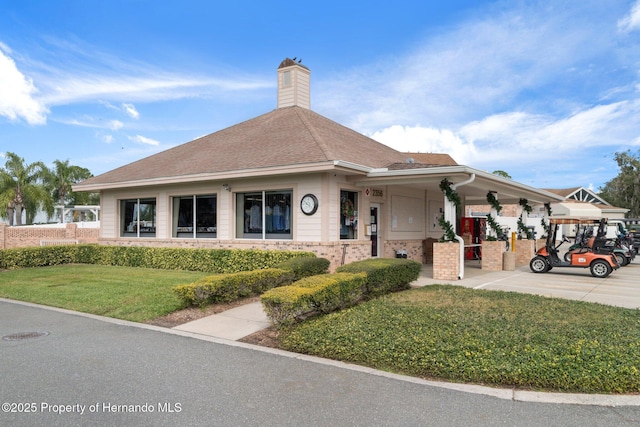 view of front of home featuring a front yard, brick siding, roof with shingles, and a chimney