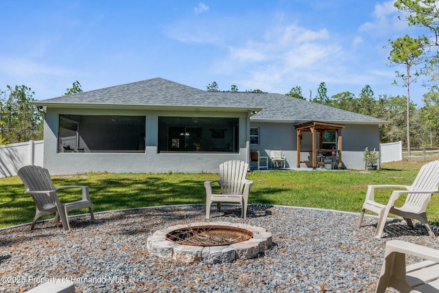 rear view of house with a shingled roof, a fire pit, a sunroom, fence, and stucco siding