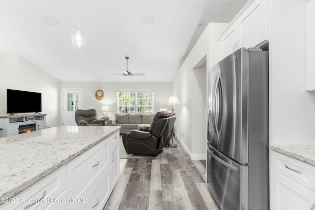 kitchen featuring stainless steel fridge with ice dispenser, open floor plan, light stone countertops, light wood-style floors, and white cabinetry