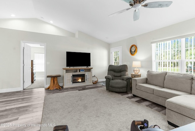 living room with lofted ceiling, wood finished floors, a glass covered fireplace, and a wealth of natural light