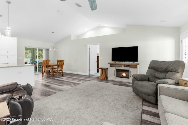 living area featuring visible vents, baseboards, a glass covered fireplace, light wood-style flooring, and vaulted ceiling