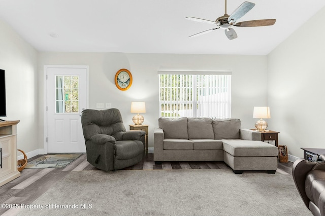 living area featuring a fireplace, ceiling fan, baseboards, and wood finished floors