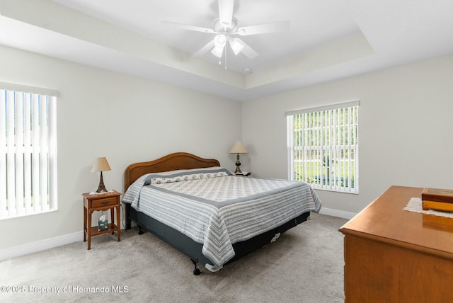 bedroom with light carpet, baseboards, a tray ceiling, and a ceiling fan