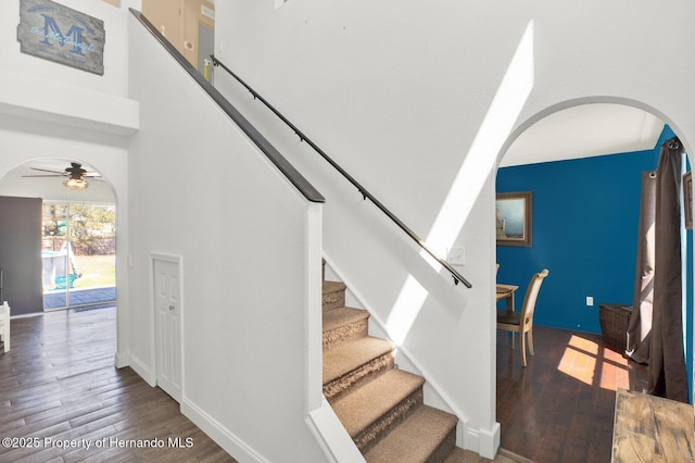 stairway featuring arched walkways, a high ceiling, wood finished floors, and baseboards