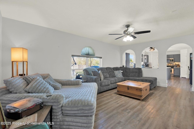 living area with arched walkways, ceiling fan, baseboards, and wood finished floors