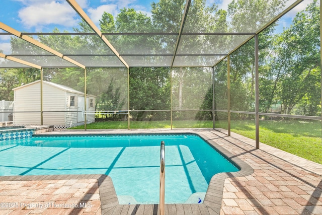 view of swimming pool featuring a storage unit, a pool with connected hot tub, a patio, glass enclosure, and an outdoor structure