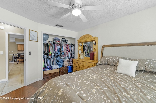 bedroom with wood finished floors, visible vents, ceiling fan, a closet, and a textured ceiling