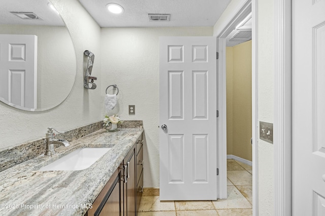 bathroom featuring vanity, a textured wall, visible vents, and a textured ceiling