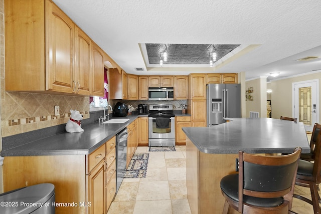 kitchen with a sink, dark countertops, stainless steel appliances, decorative backsplash, and a raised ceiling