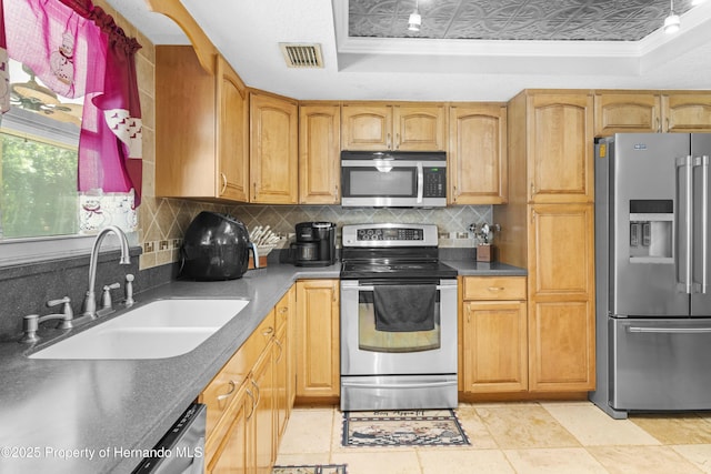 kitchen featuring visible vents, a tray ceiling, a sink, stainless steel appliances, and tasteful backsplash