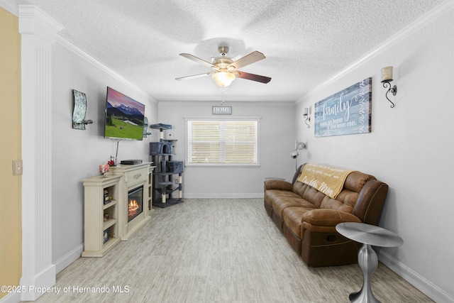 living area featuring a glass covered fireplace, crown molding, baseboards, and ceiling fan