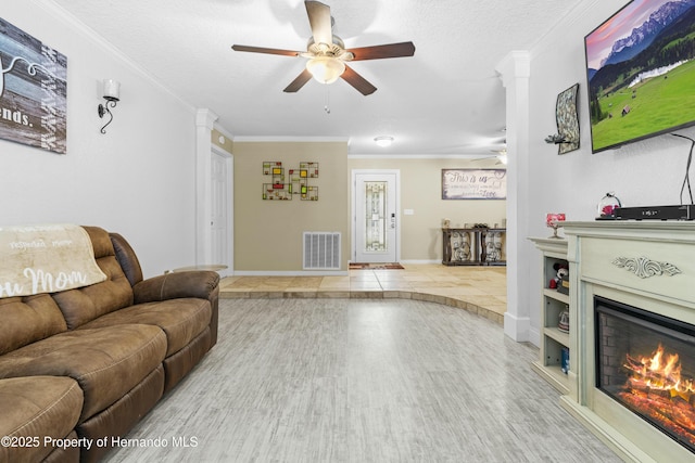 living area featuring crown molding, wood finished floors, visible vents, and a lit fireplace