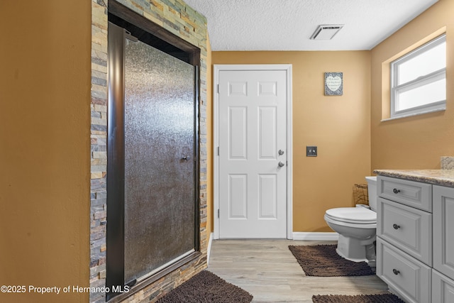 bathroom featuring wood finished floors, visible vents, a shower stall, a textured ceiling, and toilet