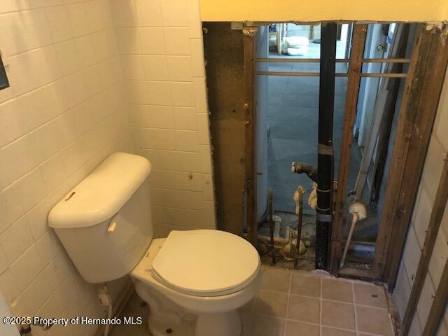 bathroom with tile patterned floors, toilet, and tile walls