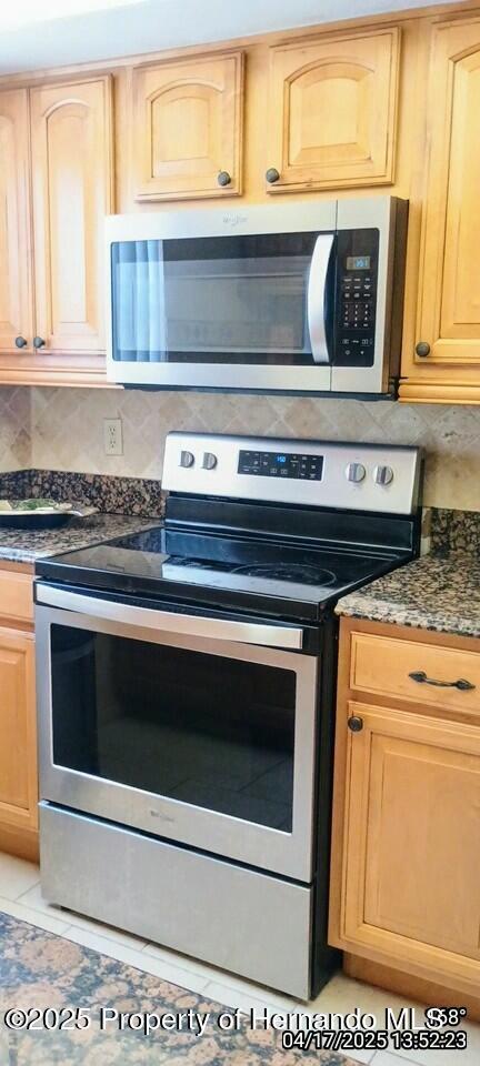 12437 Drayton Dr, Spring Hill, FL 34609 - kitchen with backsplash, light brown cabinets, light tile patterned flooring, dark stone counters, and appliances with stainless steel finishes